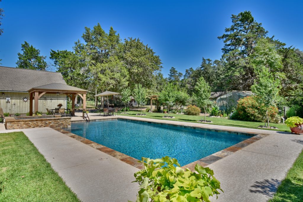 backyard swimming pool with red stone border and green landscaping