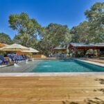 wooden deck leading to modern swimming pool with water features and lounge area