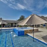 blue swimming pool with grey patio and tan umbrellas