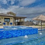 blue tile jacuzzi and swimming pool with umbrellas in countryside